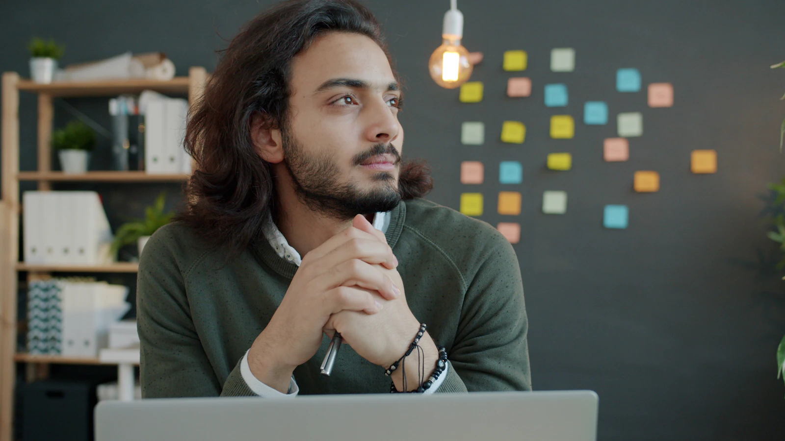 Un homme aux cheveux longs réfléchit à son bureau devant un ordinateur portable